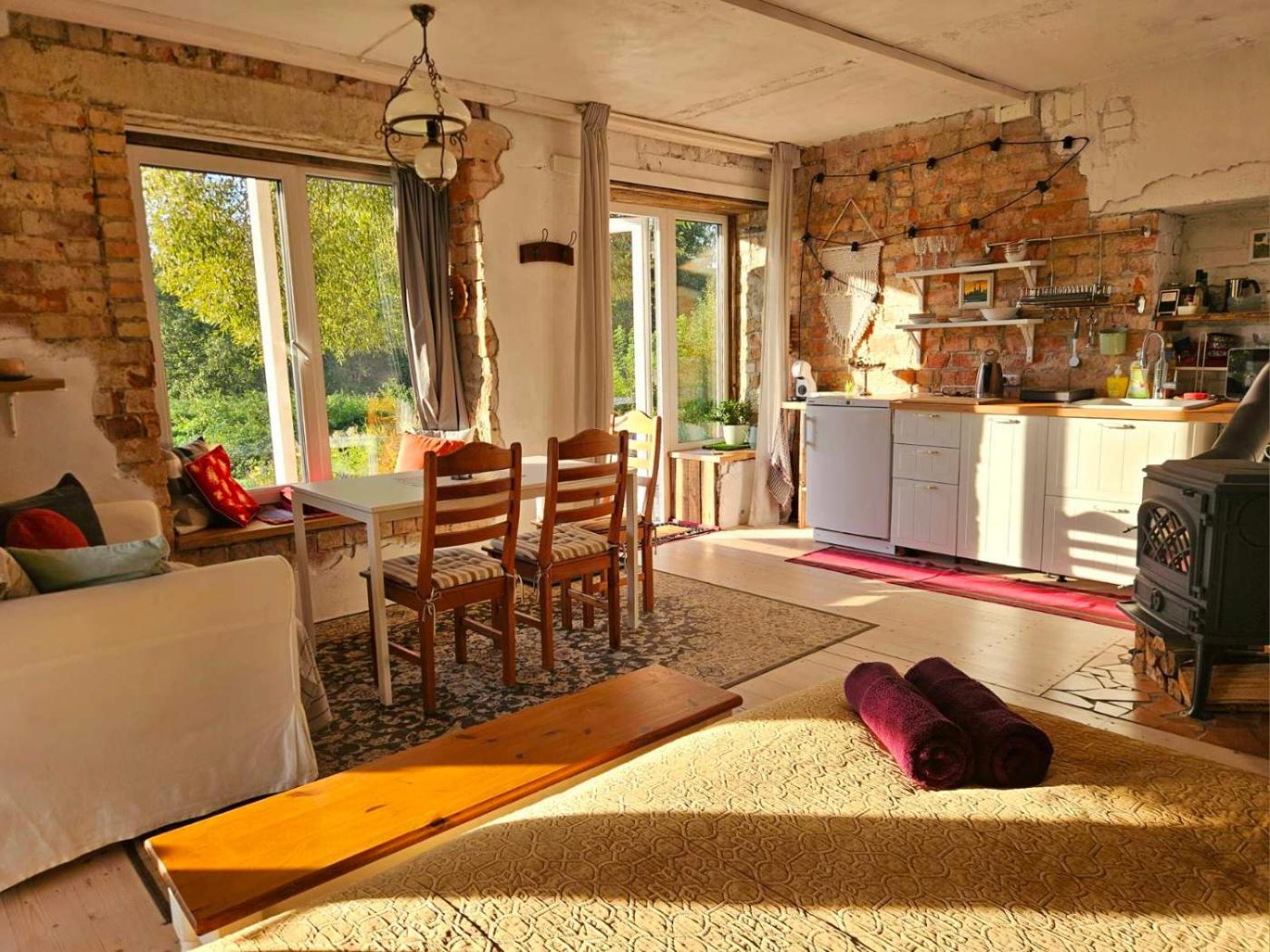 Apartamentų svetainė dieną: plytų siena, valgomojo stalas, virtuvė ir langai į sodą